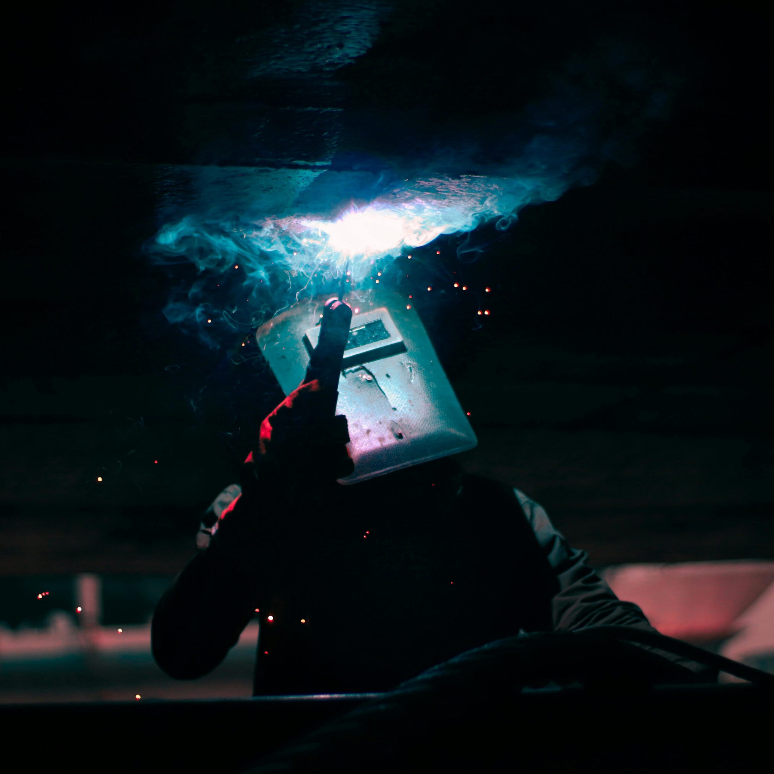 Home Silhouette of a welder working with sparks flying and smoke, showcasing safety gear.